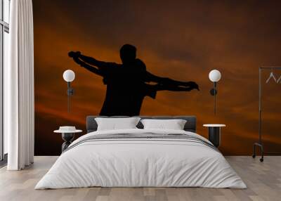 the silhouette of two people standing with their arms outstretched against a sunset sky. Wall mural