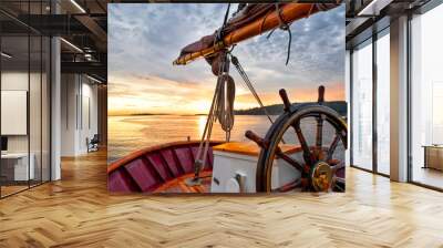 Sunrise sailing on a tall ship schooner.  Close up of steering wheel, bow and boom against a dramatic sky at dawn. Wall mural