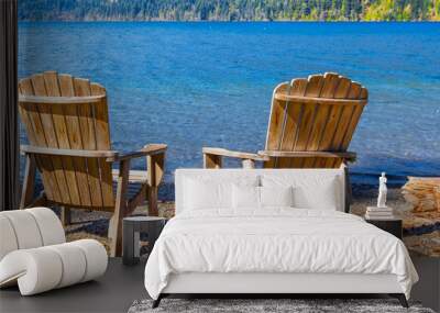 Two rustic wooden chairs by the side of a blue mountain lake Wall mural