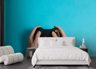 hands of a man holding a video game console controller on a blue background Wall mural