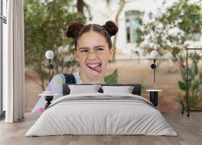 Portrait of a red haired crazy little girl with freckles laughing and sticking out her tongue in a park, concept of happiness and joy, carrying a backpack. Wall mural