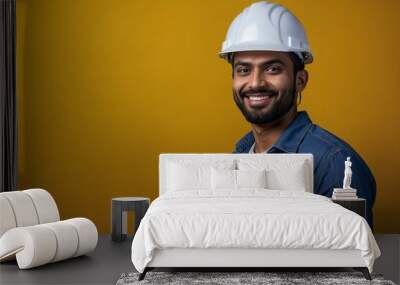 Indian engineer guy with smile on face next to empty space on a yellow background. Young handsome engineer wearing a construction helmet. Wall mural