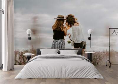 Back side shot of two young women looking at mobile phone, taking photographs in a sage flower field Wall mural