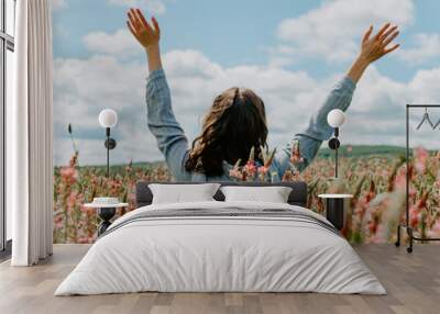 Back view of young woman in pink flower field with arms up towards the blue sky Wall mural