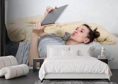 Beautiful girl looks at the tablet in bedroom. Wall mural