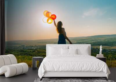 Silhouette of a young woman walking with balloons on a hill backlit by sunset golden light, concept of freedom and carelessness  Wall mural