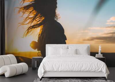 Silhouette of a young woman with her hair in motion backlit by gorgeous golden sunset sky Wall mural