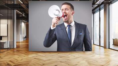 Business man screaming with a megaphone on grey background Wall mural