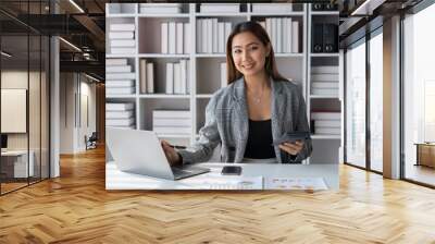 Asian businesswoman using calculator to do financial business calculations Investment with data graph document. Statistics. Laptop computer at office. lifestyle management concept. Wall mural