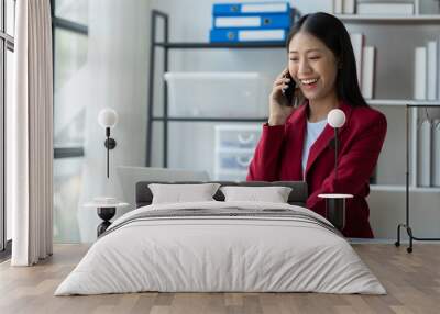 Asian businesswoman using mobile phone Laptop computer in private office to communicate through online applications and happy smile startup business ideas. Wall mural