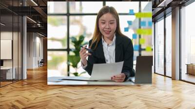 Asian businesswoman working using laptop computer in office, thinking, planning accounting analysis report with financial graphs and investment information. Financial and tax system concepts. Wall mural