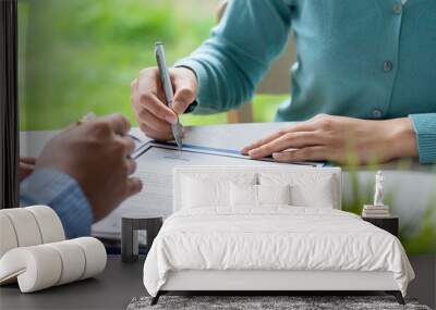 Businesswoman signing a document or application form in a folder, Woman signing document with pen on a desk at home Wall mural