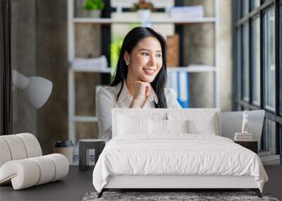 Portrait of a beautiful cheerful Asian businesswoman sitting at her desk with a cup of coffee while taking a break with a happy smile in her upcoming successful business. Wall mural