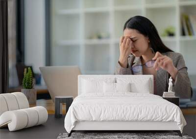 Tired young woman freelance worker rubbing her eyes while sitting in front of laptop computer and working on promising project Wall mural