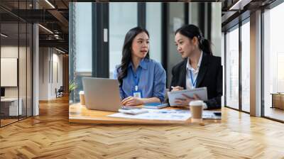 Two Asian businesswomen discuss investment project work and planning strategy Brainstorm together Find information online on iPad Laptop and tablet for making reports and summarizing business results Wall mural