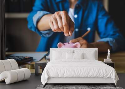 woman holds a coin in a pig-shaped piggy bank to save money for the future. after retirement and record keeping of income, expenditure, savings and financial concepts. Wall mural