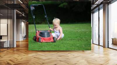 Funny little baby girl is playing outside with lawn machine  Wall mural