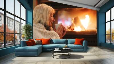 Senior woman relaxing at by fireplace Wall mural