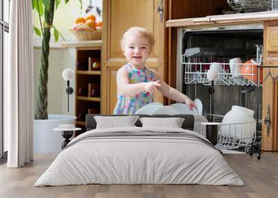 toddler girl helping in kitchen taking plates out of dish washer Wall mural