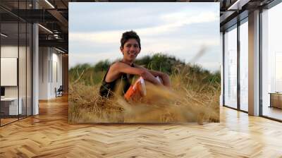 Young happy teenage boy sitting at hay field and smiling outdoors Wall mural