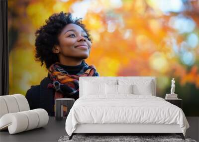 African-American woman in casual clothing, walking through a park during autumn, surrounded by colorful leaves, with a serene and content expression Wall mural