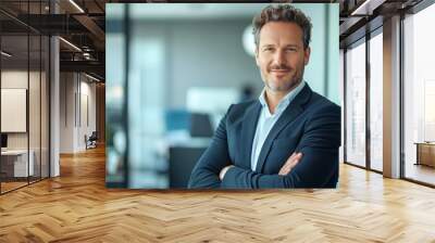 Handsome businessman standing with arms crossed, looking at the camera with a smile, bright office environment Close-up photo with clean background Wall mural