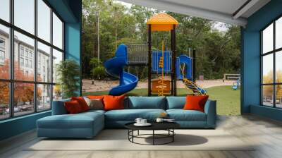 Children plastic house with yellow roof and blue slide with tropical jungle in the background and fake green grass on a cloudy day  Wall mural