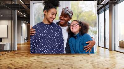 Smiling mother embracing two daughters at home Wall mural