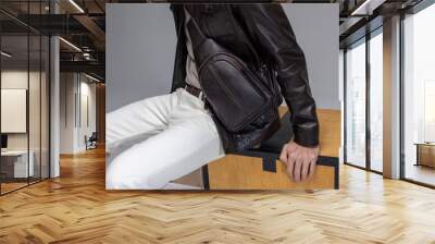 The faceless male model is wearing a dark leather bag, a leather jacket and white jeans. Close-up studio shot Wall mural