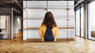 Rear view of young woman standing in front of empty shelf in a supermarket Wall mural