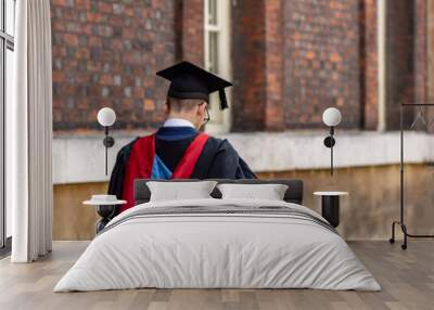 Graduate man student wearing graduation hat and gown at university camp Wall mural