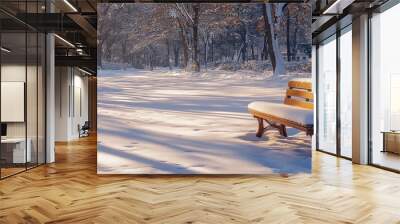 A wooden bench covered in snow sits in a snowy forest path. Wall mural