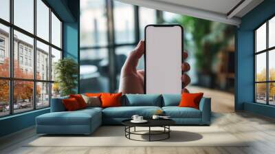 A man's hand holding a smartphone in modern office with white blank screen, First person view Wall mural