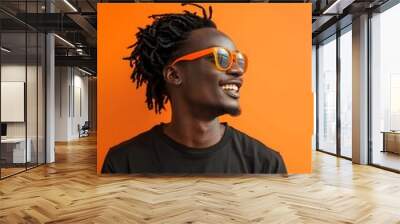 Confident young African American man smiling and using smartphone in studio with orange background Wall mural