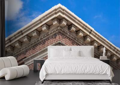 Upward view of the decorative roof cornice on a vintage red urban brick building, with blue sky background Wall mural