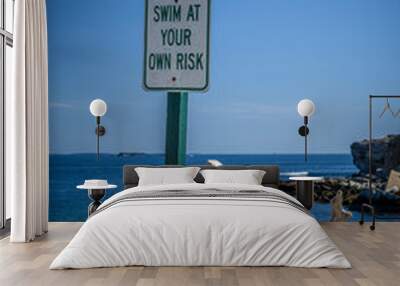 Swim at your own risk sign with a beautiful cove and sunshine as a backdrop Wall mural