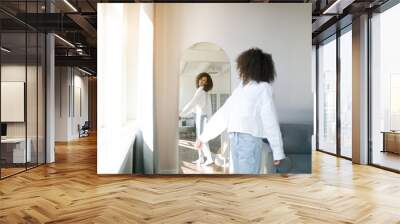 Cute african american girl choosing clothes to wear in front of mirror in i the living room. Morning wake up concept        Wall mural