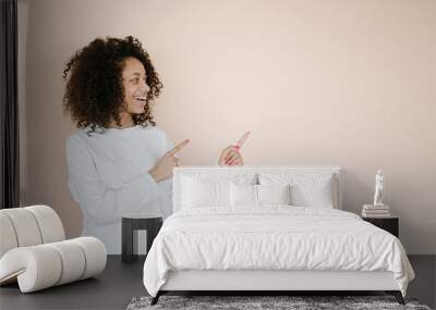 Portrait of smiling young african american woman giving information, showing way, pointing fingers right at copy space aside, standing upbeat against brown background Wall mural