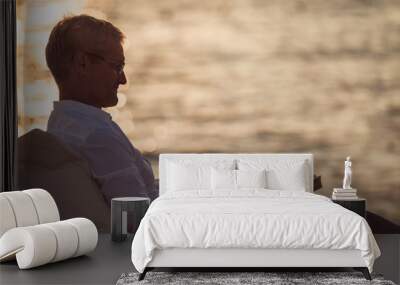 Senior man reading a book lying on deck chair on the beach during sunset Wall mural