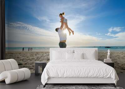 Father lifting daughter, having fun on the beach. A smiling young man playing with his cute little girl on vacation. Fun family vacation Wall mural