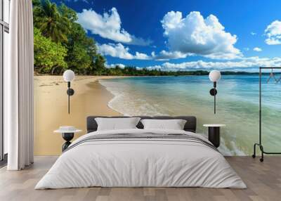 A pristine sandy beach with clear blue water and a beautiful sky filled with white, fluffy clouds, surrounded by vibrant greenery and palm trees. Wall mural