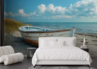 An old, weathered boat rests on a sandy beach, with a serene blue sky and calm sea in the background Wall mural