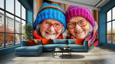 Close-up of two elderly women smiling warmly and wearing vibrant, colorful hats and scarves, highlighting their close friendship and mutual affection. Wall mural