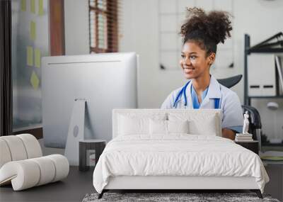 African american female doctor sitting in front of computer at her clinic office Wall mural