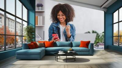 successful and exciting african american businesswoman Young woman excited to win on her smartphone at work. Wall mural