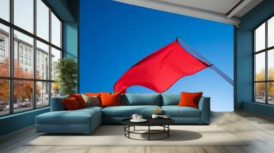 A red flag in the wind isolated on bright blue sky background. Wall mural