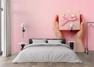 A pair of hands holding a beautifully wrapped pink gift box on a soft pink background, perfect for celebrations and special occasions. Wall mural