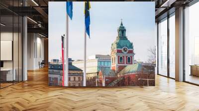 city streets view from bottom to top of ancient church green tower with golden cross at the same peak; tower facade in red and with clocks above Wall mural