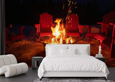 Cozy/romantic evening scene of warming bonfire on snow in winter with red chairs around. Canadian symbols of bear, paw and tree on the fire container. Banff National Park, Alberta, Canada Wall mural