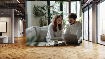 Happy couple working on laptop, bright living room, casual attire, green plants, natural light, cozy home environment, copy space
 Wall mural